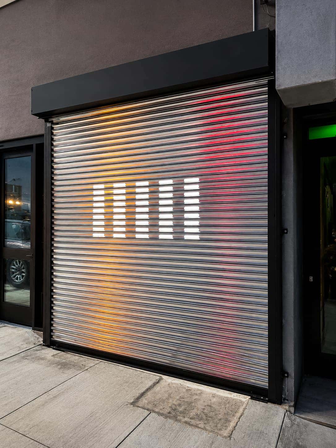 Perforated storefront roll up gate seen at an angle with interior light through the slots