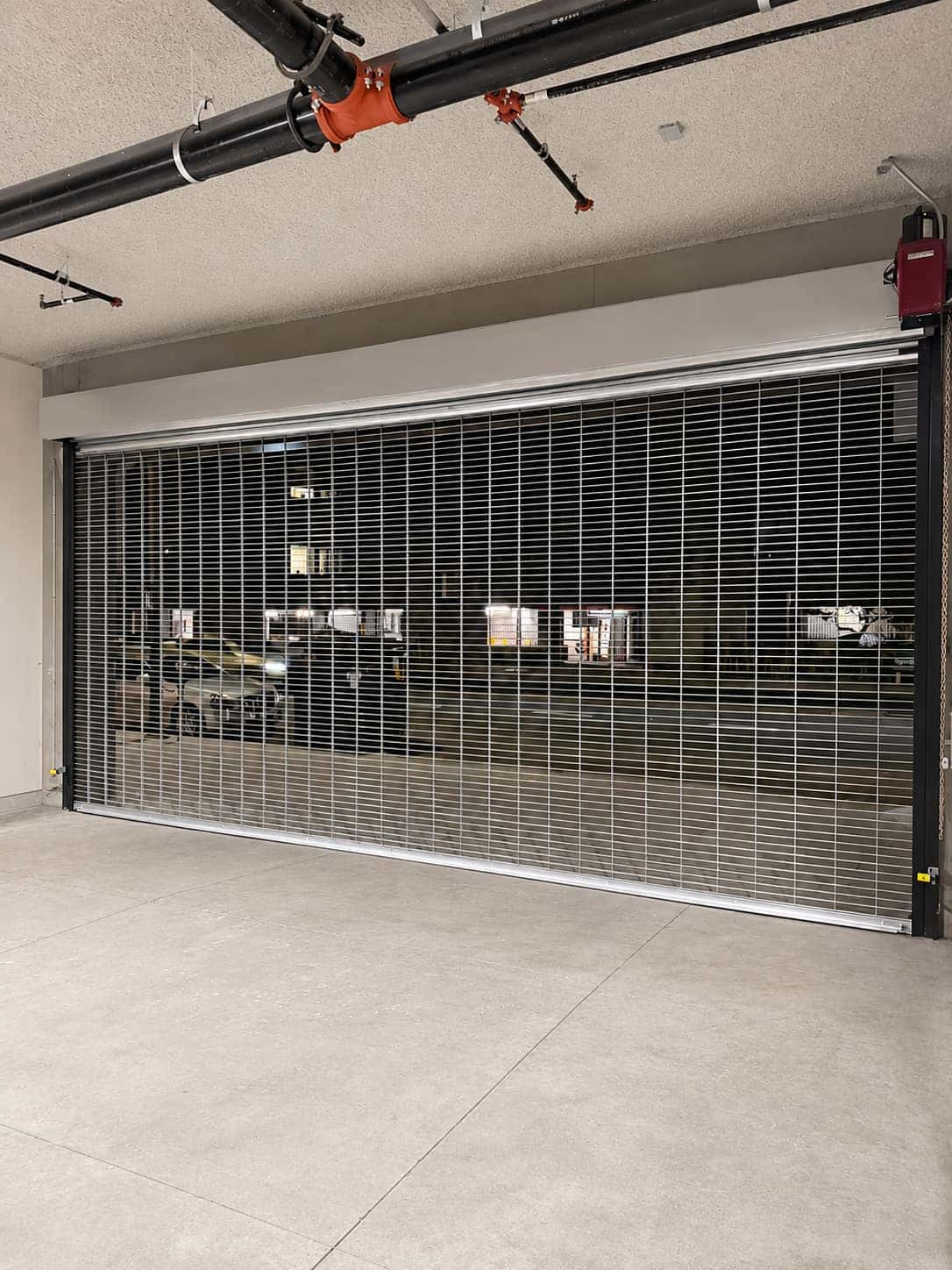Open-air rolling security grille with a motor operator securing a parking structure entrance