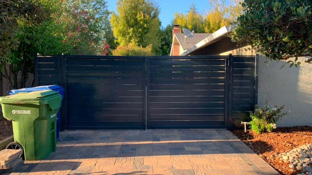 Black horizontal-slat double swing driveway gate on stamped concrete