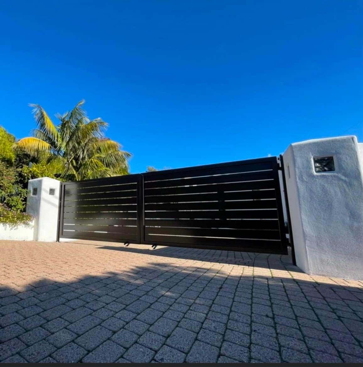 Black slat sliding driveway gate traveling along the fence line at a Bay Area home