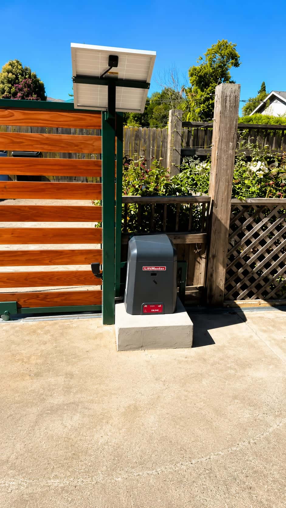 Solar-powered slide gate operator with a roof-mounted panel beside a redwood gate