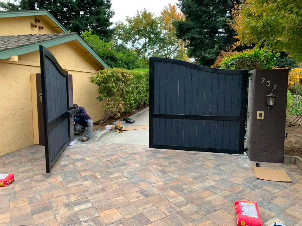 Arched wood and black steel driveway gate between masonry columns