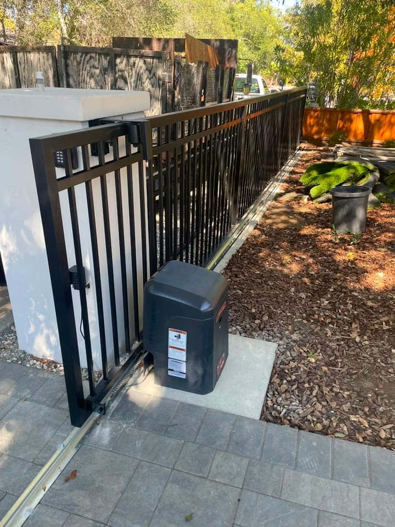 Slide gate operator beside a commercial iron gate with an entry keypad